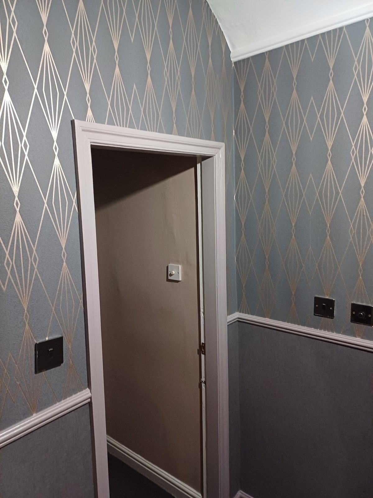 A hallway papered in blue-grey and gold diamond wallpaper above a grey dado
