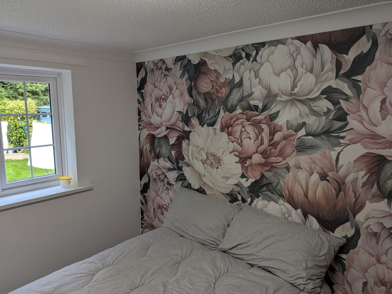 A bedroom with a large floral peony wallpaper feature wall behind the bed