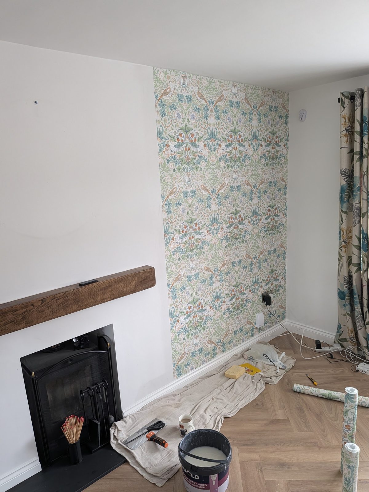 Wallpaper going up on a chimney breast, with the decorating kit on the floor