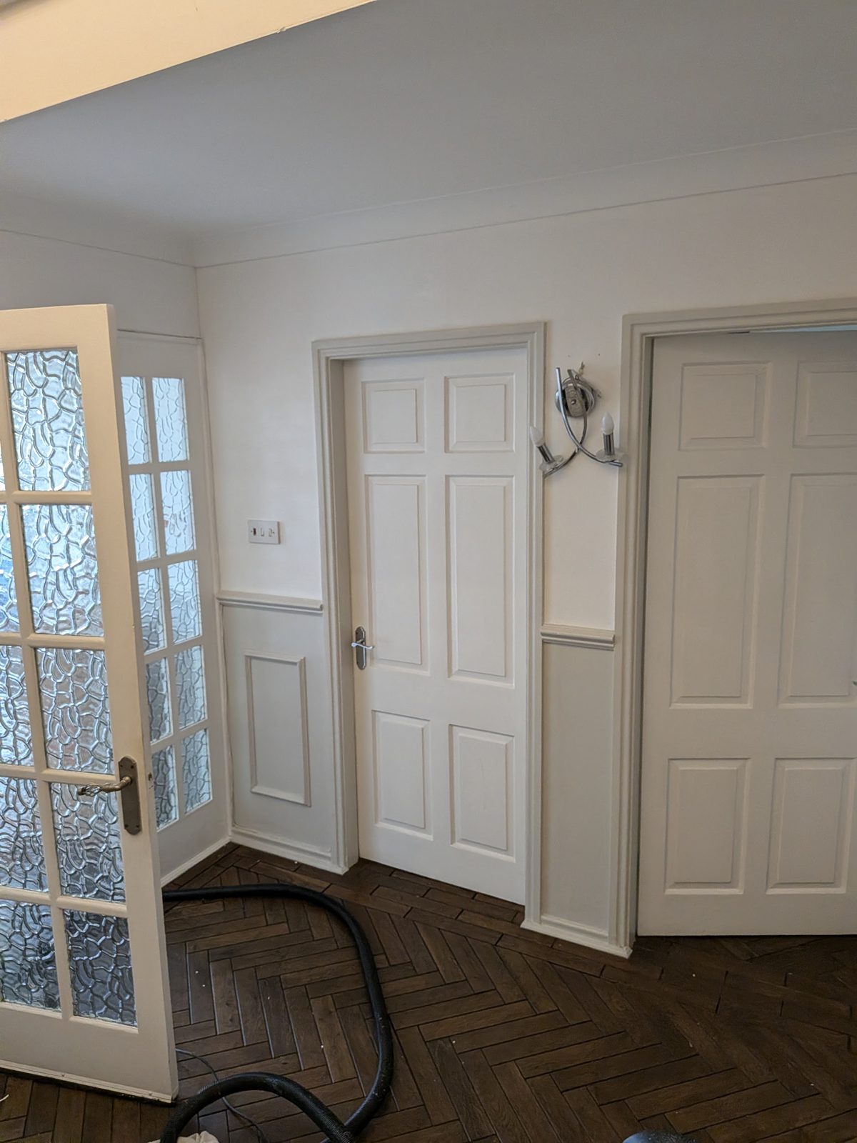 A hallway with white panelled doors and dado, freshly painted, with the vacuum cleaner on the wood floor